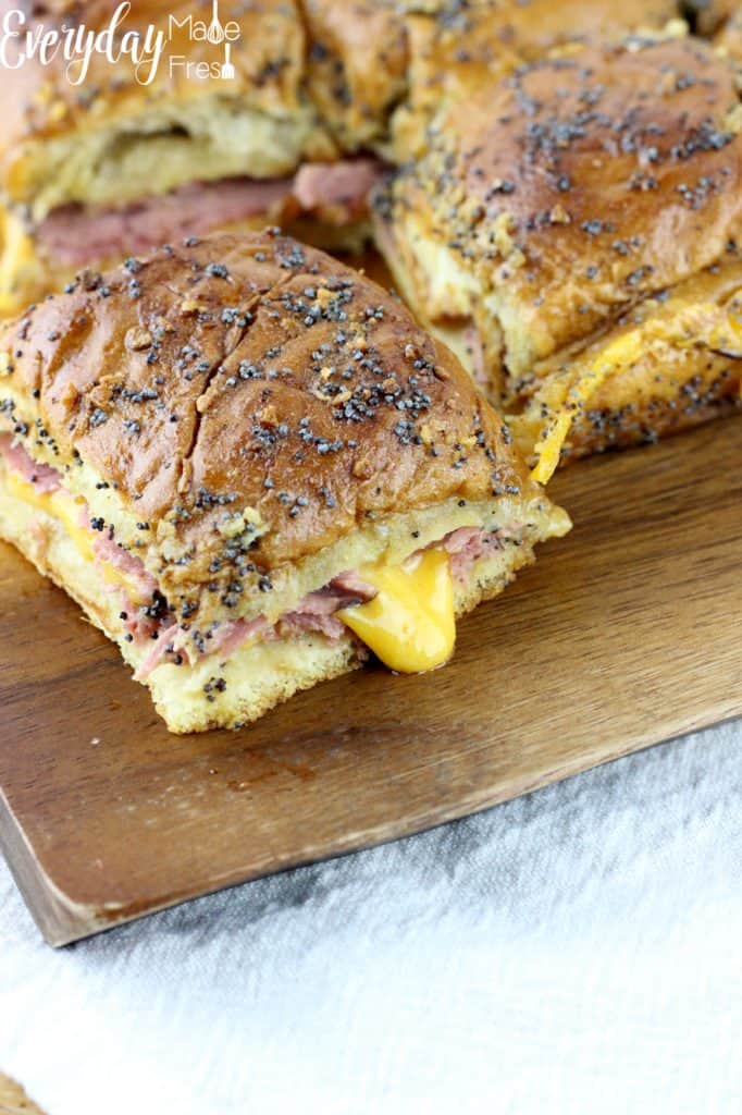 small sandwich with a toasted bun like top, coated in poppy seeds. inside the sandwich which you can see oozing out the sides is roast beef and melted cheddar cheese.