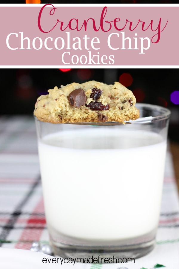 a cranberry chocolate chip cookie with a bite mark, balanced on the rim of a glass of milk